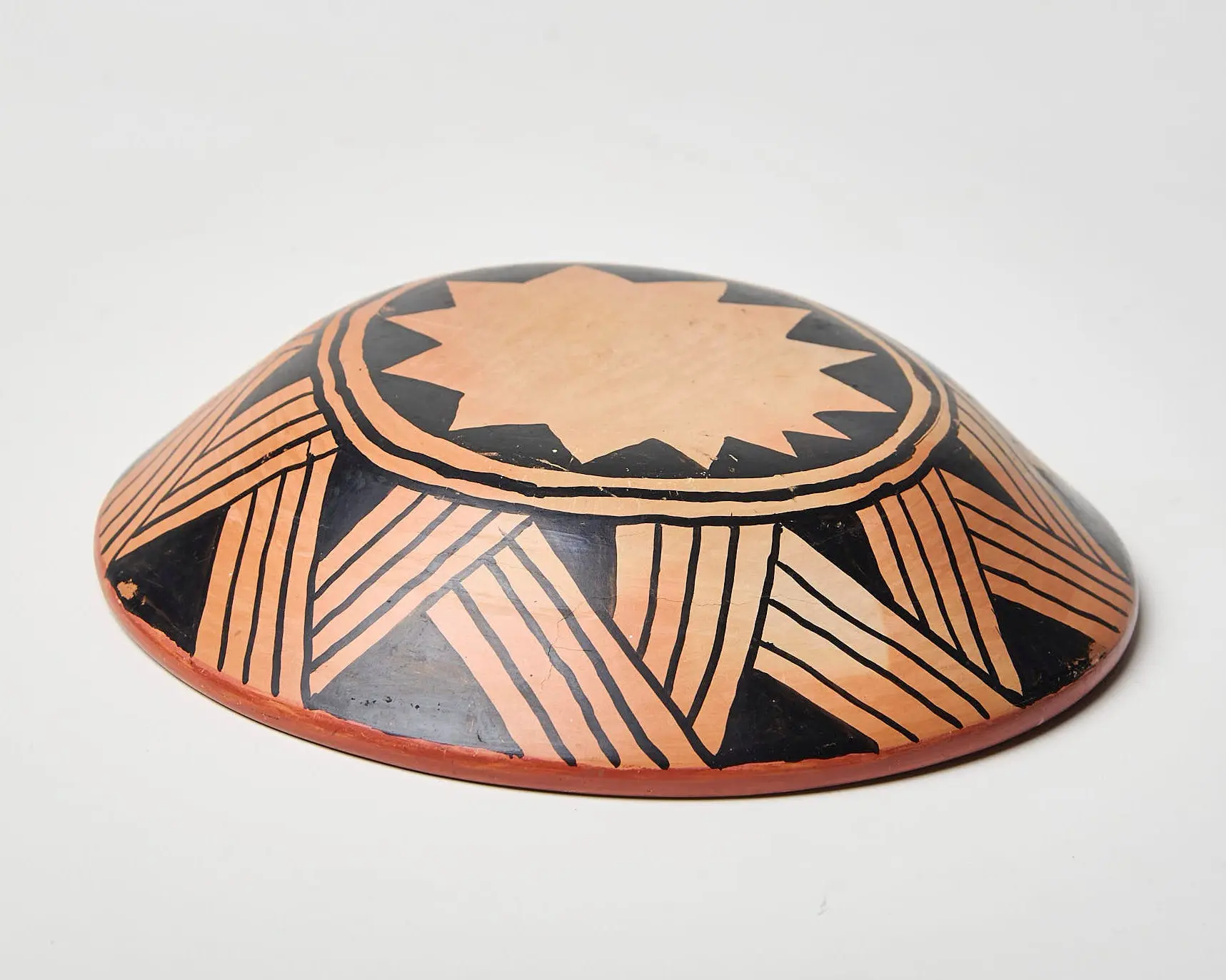 Recipiente cerâmico Wauja muito baixo e circular, com exterior pintado em preto e bege e interior vermelho-terra.